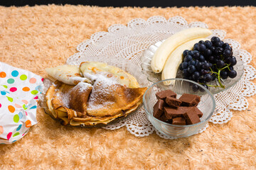 A delightful arrangement of pancakes dusted with powdered sugar, fresh fruit including bananas and...