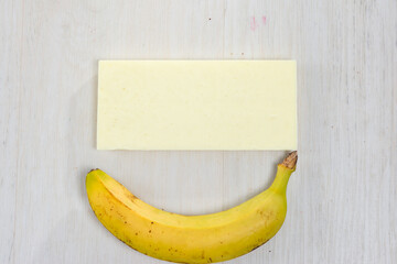 A single ripe banana positioned beneath a rectangular block of an unidentified white material. Both...
