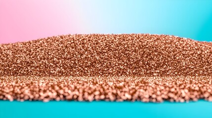 A mound of rose-gold metallic particles rests on a teal surface against a pink and blue gradient background