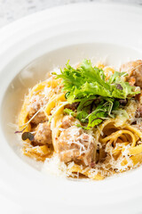 A plate of creamy pasta with meatballs, garnished with fresh greens and grated cheese, served on a textured stone surface. Perfect for culinary presentations, restaurant menus, and food advertising.