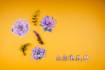 A yellow background showcases delicate purple flowers and greenery alongside a row of small white house figurines