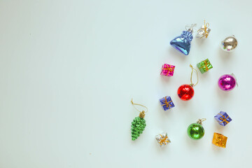 A collection of colorful Christmas ornaments, including baubles, gift boxes, and a small tree, is scattered on a light background, New year is coming