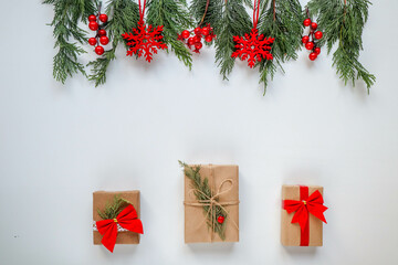 A stack of wrapped Christmas gifts with red ribbons is placed under a garland decorated with red berries, snowflakes, a white background, New year is coming