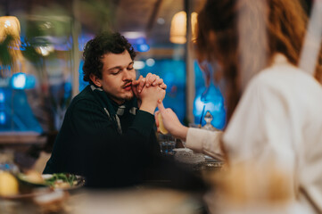 A man deep in thought while holding hands with another person in a softly lit restaurant...
