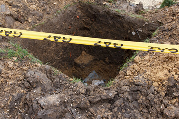 Construction site gas line warning tape across deep excavation hole in ground