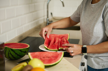 In a bright kitchen setting, a woman cuts ripe watermelon into slices, embracing healthy eating. Vibrant fruit and a clean countertop underscore a focus on lifestyle and freshness.