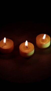 Una toma de cerca de tres velas amarillas  con fuego en la oscuridad