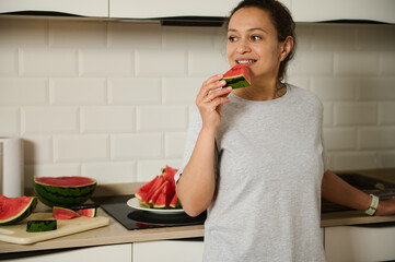 A cheerful moment captured as a woman enjoys a slice of refreshing watermelon in a cozy kitchen....