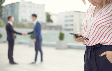 Woman is holding a mobile phone in the background handshake of two business men. Blurred business...
