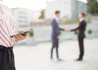 Woman is holding a mobile phone in the background handshake of two business men. Blurred business...