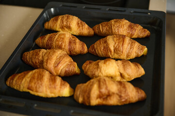 Golden croissants are freshly baked, displayed on a tray in a warm, inviting kitchen ambiance, emphasizing culinary skills and homemade delights.