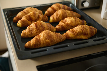Golden brown croissants rest on a baking tray in a cozy kitchen setting, showcasing homemade baking...