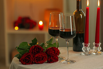 Glasses of red wine, burning candles and roses on table in restaurant. Romantic dinner