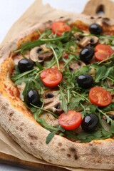 Tasty pizza with cherry tomatoes, black olives, mushrooms and arugula on white table, closeup