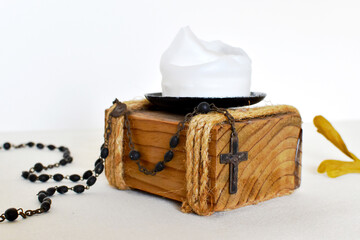 Dark rosary for prayers on a light background, yellow dried flower and wooden candlestick with white candle