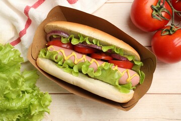 Tasty hot dog with tomatoes, onion, lettuce and mustard on wooden table, flat lay