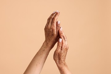 Woman applying body scrub onto her hands on beige background, closeup