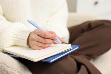 Woman writing in planner on armchair indoors, closeup