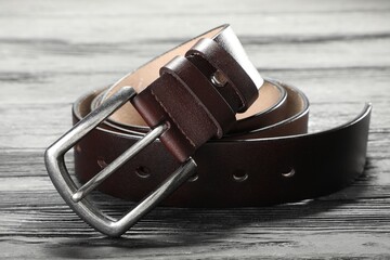 One brown leather belt on wooden table, closeup