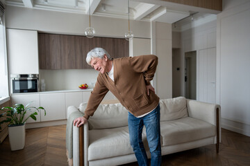 Sad senior man hunches in agony after severe back spasm by lumbar disc herniation. Vertebral nerve...