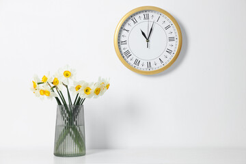 Beautiful daffodils in vase on white table and clock indoors