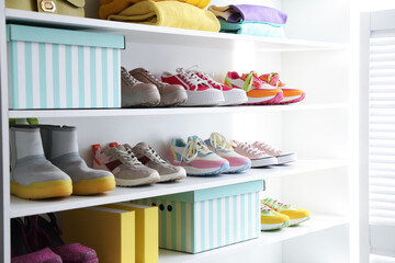 Different footwear and clothes on shelves indoors, closeup. Shoe storage
