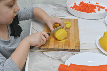 a little girl at the table cuts boiled potatoes into a salad.