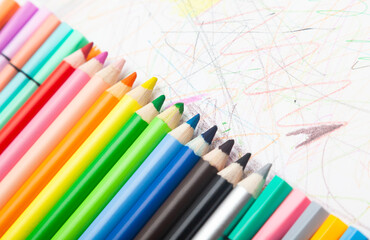 Multi-colored pencils lie on white paper drawn with multi-colored curved lines.