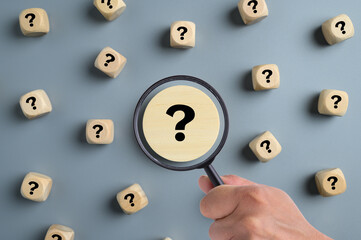 Hand holding magnifying glass over question mark scattered across background, Troubleshooting,...