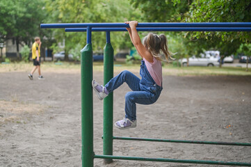 Fototapeta premium A little girl wants to climb a crossbar