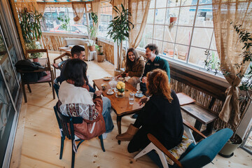 Group of friends enjoying coffee and conversation in a cozy, warmly lit setting, surrounded by natural decor and relaxed ambiance, fostering a joyful and welcoming atmosphere during their gathering.
