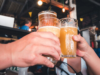 Three people clinking glasses of cold, hazy craft beer in a lively bar setting, celebrating friendship and good times.