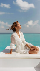 Relaxing by the ocean in a white robe with a serene expression and gentle breeze under a bright blue sky