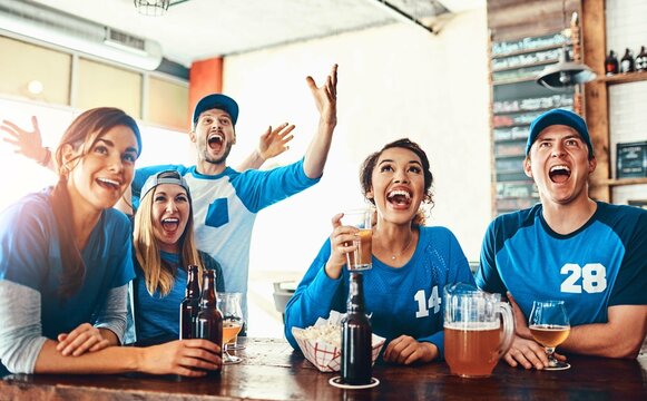 Beer, sports and fans in pub for winning game with goal for celebration in support together. Excited, cheering and group of people drink alcohol and watch broadcast television of team match in bar.