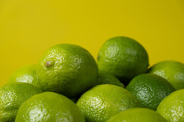 Whole fresh limes fruit on yellow background close-up.