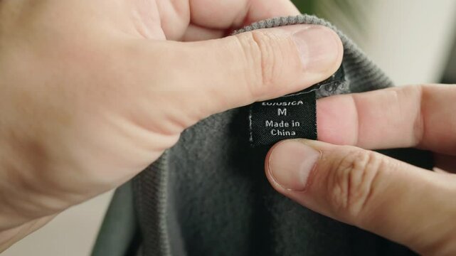 Close-up of hands holding a black clothing label marked "Made in China"