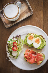 Delicious breakfast featuring avocado toast and smoked salmon with coffee on a wooden table, flatlay.