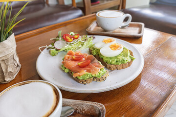 Breakfast dish featuring smoked salmon and avocado toast with coffee served in a cozy cafe setting