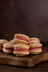 Vegan homemade caramel macarons with raspberry cream on shea butter on a wooden table. Sugar, lactose and gluten free. Vertical orientation.