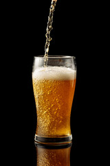 Pouring beer into a glass on a black reflective background.