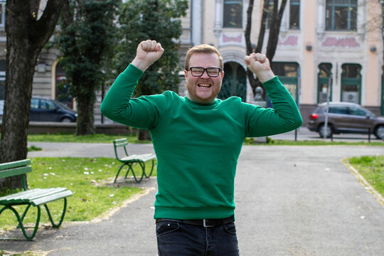 Joyful Caucasian man in emerald sweater celebrates in urban park, embodying World Laughter Days exuberant spirit and serendipitous joy