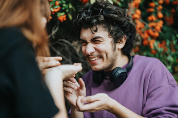 A joyful young man with headphones laughs heartily with friends in a colorful garden setting. The mood is cheerful and carefree, capturing the essence of friendship and happiness.