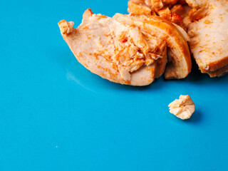 A tray of Cajun style chicken is on a blue background. The chicken is cut into pieces. Small...