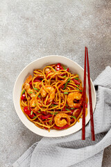 udon stir-fry shrimp noodles with red bell pepper and green onion, served in a black bowl, with chopsticks, gray background,