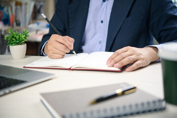 Naklejka premium Corporate worker writing goals in personal notebook, working at organized desk with green plant. Productivity, strategy, and focus concept for professionals.