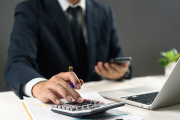 Businessman calculating financial data with calculator and smartphone at office desk. Concept of...