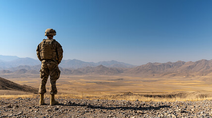 soldier stands rocky terrain, gazing vast valley surrounded by mountains clear blue sky. scene conveys sense of solitude