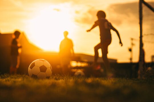 Action sport outdoors of kids having fun playing soccer football for exercise in community rural area under the twilight sunset sky.