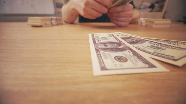 A close-up of a man's hands fanning out $100 bills. Shot at a wide angle.