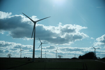 A highly detailed, professional photograph of the sun is shining behind the windmills captured with artistic lighting and excellent composition. the scene features under calm and cool conditions.